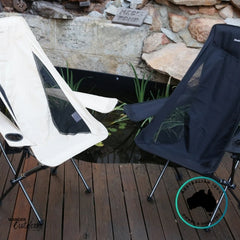 Beige and black Dhubite Outdoors compact camp chairs side by side on a timber deck beside a pond, showing colour options and mesh ventilation panels.