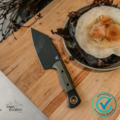 Benchmade Station Knife on chopping board beside plated meal, showcasing black DLC blade and olive drab G10 handle.