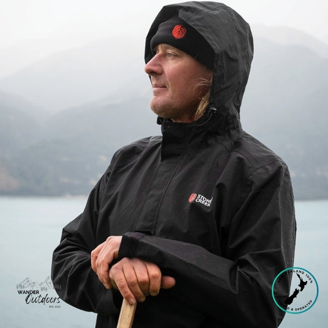 Person wearing a Stoney Creek Recreational (Stow it) Jacket in Black, holding a paddle, standing in front of a body of water.