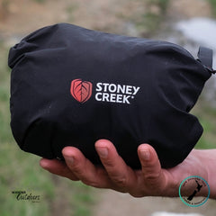 Packed, ready and compact Stoney Creek Recreational (Stow it) Jacket in Black held in a hand with a blurred natural background