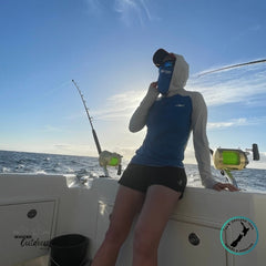 Person on a boat wearing a blue cap and fishing outfit with a clear sky and ocean background.
