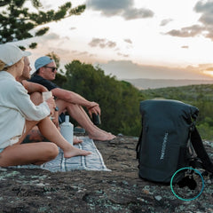 three people sitting on a rock with a scenic view, an Aussie Pal backpack in the foreground.