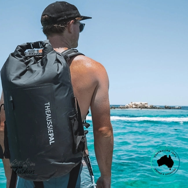 Person with a black backpack labeled 'The Aussie Pal' by the ocean.