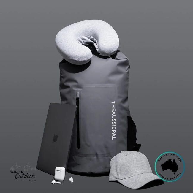 Gray backpack with travel pillow, phone case, earbuds, and cap on a gray background