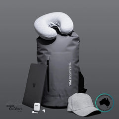 Gray backpack with travel pillow, phone case, earbuds, and cap on a gray background