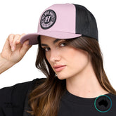 Model wearing The Mad Hueys Living Hueys Twill Trucker Hat in mauve and black, showing front logo and curved brim.