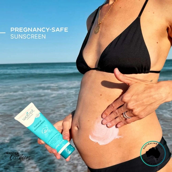 Pregnant woman applying Wotnot Naturals SPF 50 Zinc Sunscreen Matte Finish to her belly at the beach.
