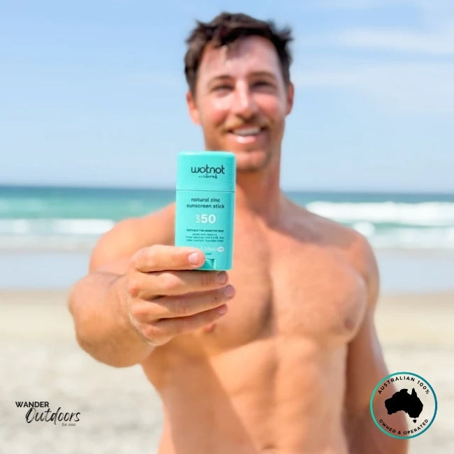 Man holding Wotnot Naturals SPF 50 Zinc Sunscreen Stick at the beach with ocean in background.