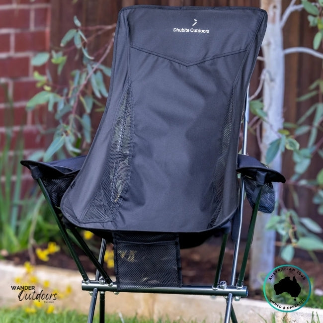 Black Dhubite Outdoors compact camp chair with mesh ventilation and armrests, photographed outdoors against a wooden fence and native plants.