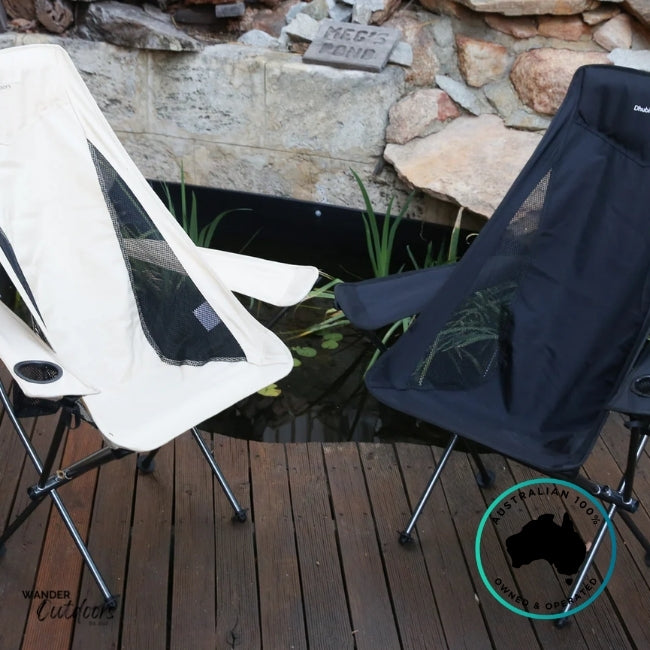Beige and black Dhubite Outdoors compact camp chairs side by side on a timber deck beside a pond, showing colour options and mesh ventilation panels.