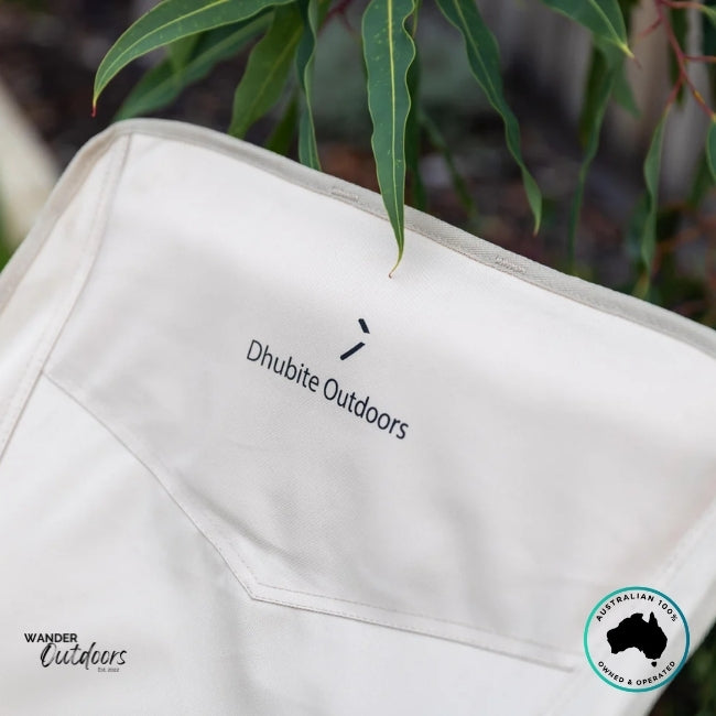 Close-up of the Dhubite Outdoors logo stitched on the beige camp chair backrest with gum leaves in the background.
