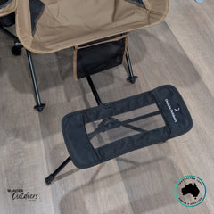 Close-up of the Dhubite Outdoors Camp Chair Foot Rest in black mesh fabric, attached to the base of the tan chair, highlighting adjustable frame and matching materials.