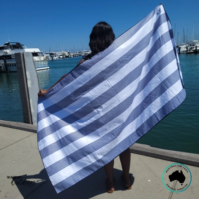 Person standing by the marina holding Newlyfe Signature Amalfi Navy Towel open to show full size and design.