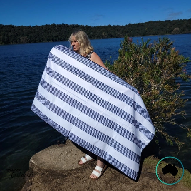 Person by the water with Newlyfe Signature Amalfi Navy Towel draped around shoulders, boats visible in background.
