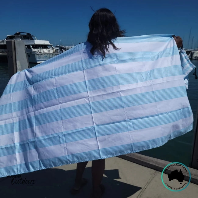 Person by the marina with the Newlyfe Signature Calvi Sky Blue Towel draped across their back, showing its oversized design and soft finish.