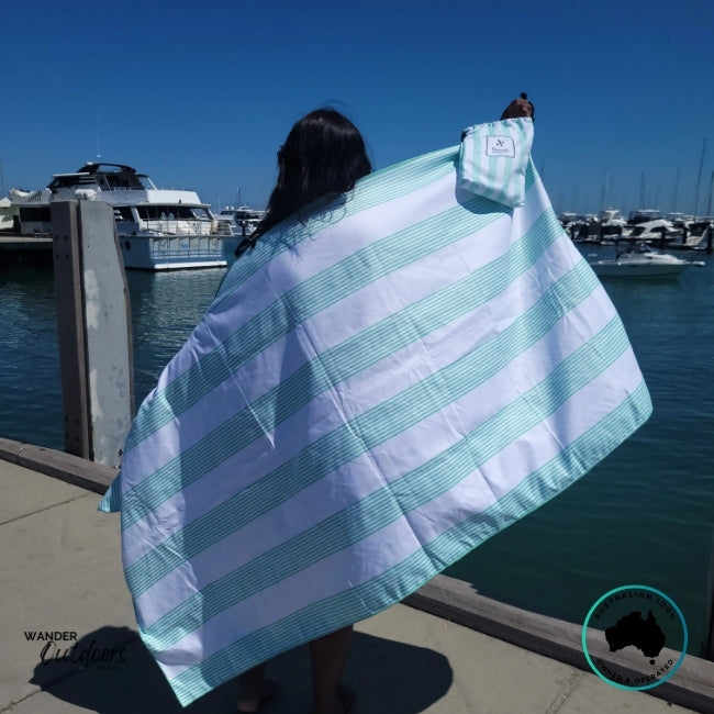 Person holding the Newlyfe Signature Milos Mint Towel and matching pouch at the marina with boats in the background.