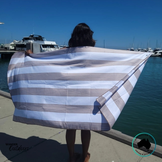 Person by the water holding the Newlyfe Signature Piha Brown Towel showing oversized fit and stripe detail.