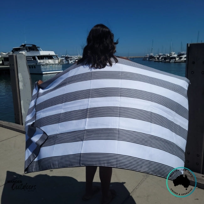 Person standing by the waterfront with the Newlyfe Signature Santorini Black Towel draped across their back.