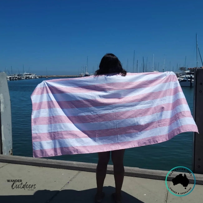 Person holding Newlyfe Signature Sanur Pink Towel at the jetty overlooking calm blue water.
