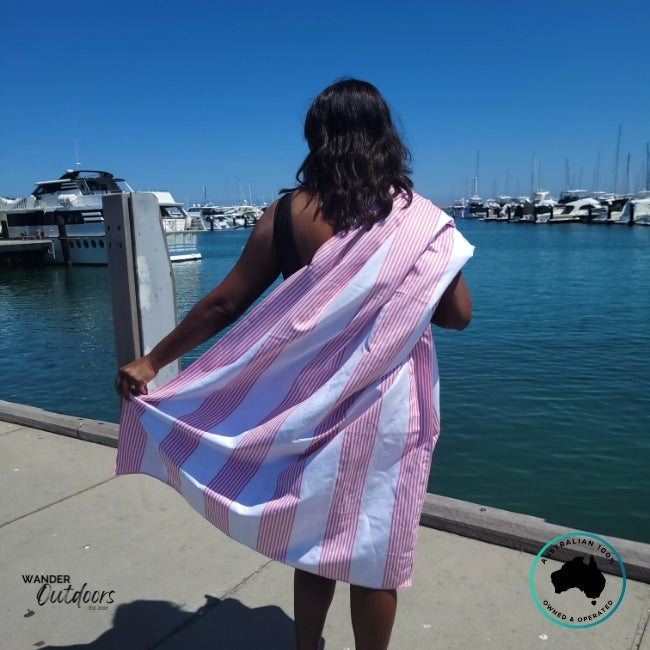 Person standing by the marina with Newlyfe Signature Sanur Pink Towel draped around shoulders, boats in background.