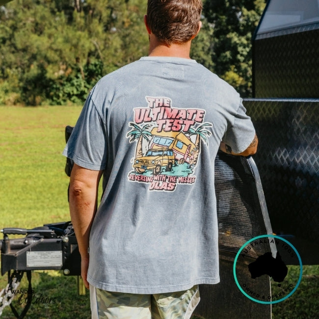 Person wearing a gray t-shirt with a graphic design, standing next to a caravan.
