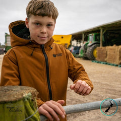 Young boy in a brown jacket standing in front of farm equipment