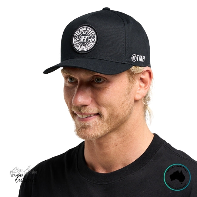 Man wearing a black cap with  The Mad Hueys Logo on a white background