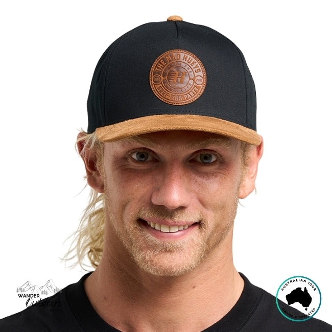 Man wearing a black cap with a brown The Mad Hueys New Suede Logo on a white background