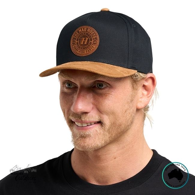 Man wearing a black and brown cap with The Mad Hueys New Suede Logo on a white background