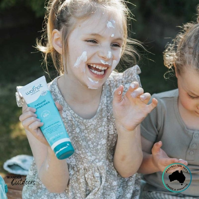 Two children laughing with sunscreen on their faces, holding Wotnot Naturals SPF 50 Sunscreen.