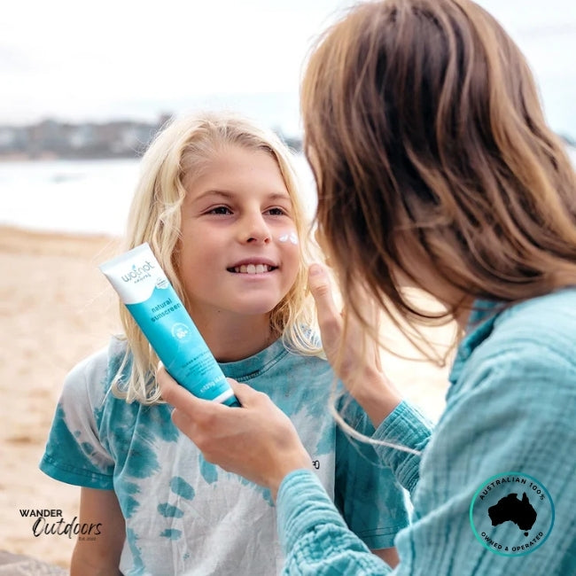 Mother applying Wotnot Naturals SPF 50 Sunscreen to her child’s face at the beach.