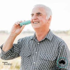 Older man smiling while applying Wotnot Naturals SPF 50 Zinc Sunscreen Stick to his face outdoors.